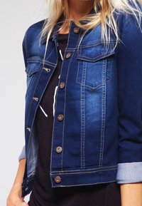 Denimjacka i mörkblått med två bröstfickor, knapplist fram och uppvikta ärmslut. Har kontrasterande sömmar och subtila blekningar.