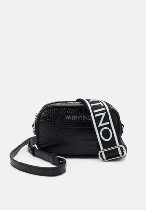 Czarna torba ze skóry z tłoczeniem imitującym skórę krokodyla, z srebrnym zamkiem błyskawicznym i białym paskiem z logo, o prostokątnym kształcie i teksturowanej powierzchni.