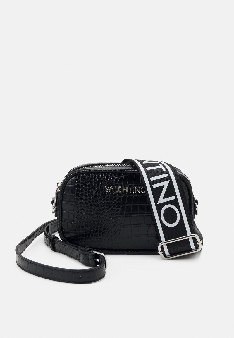 Svart krokodil präglad läderväska med silverfärgad dragkedja och märkt vit rem, med en rektangulär form och strukturerad yta.