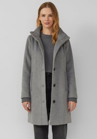 Grijze wollen jas met een hoge kraag, geribbelde accenten, knoopsluiting en zijzakken, gecombineerd met een bijpassende trui en donkere broek.