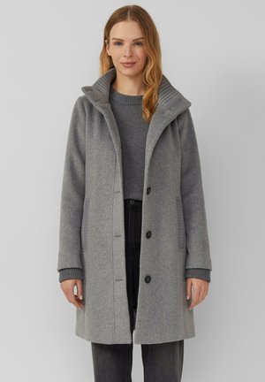 Grau wollener Mantel mit hohem Kragen, gerippten Akzenten, Knopfverschluss und Seitentaschen, kombiniert mit einem passenden Pullover und dunklen Hosen.