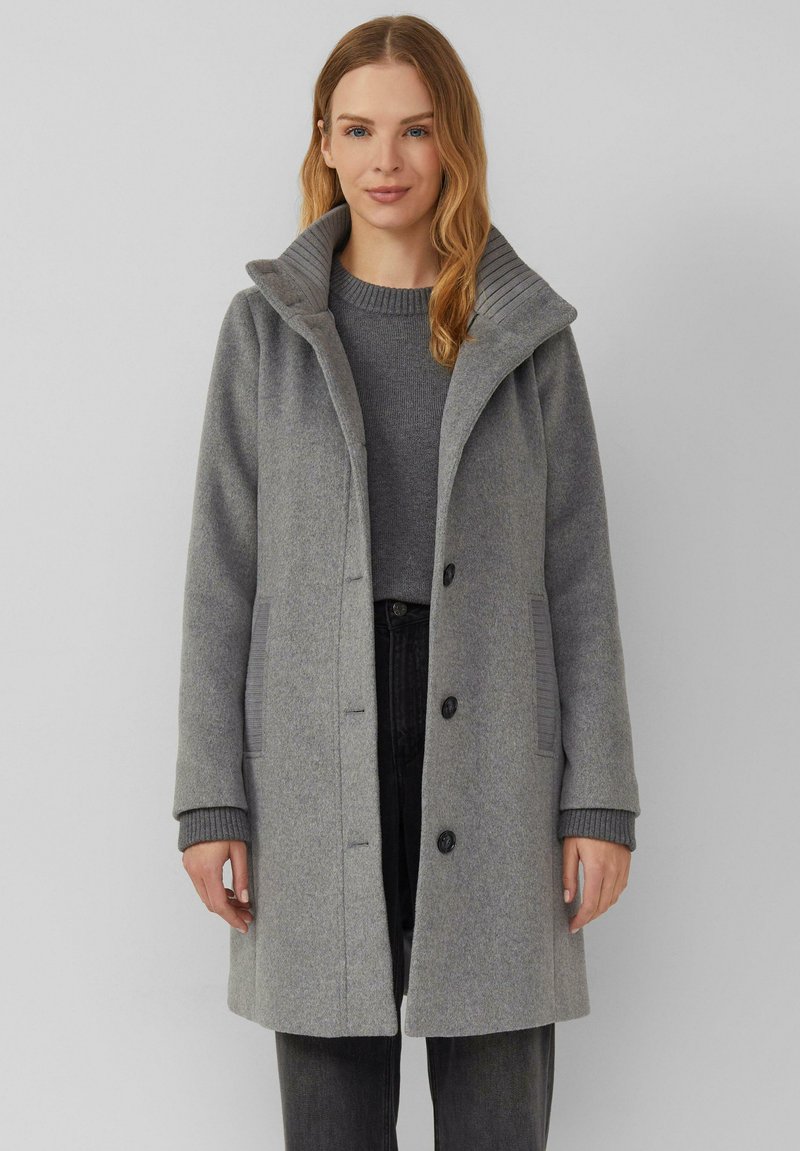 Grijze wollen jas met een hoge kraag, geribbelde accenten, knoopsluiting en zijzakken, gecombineerd met een bijpassende trui en donkere broek.