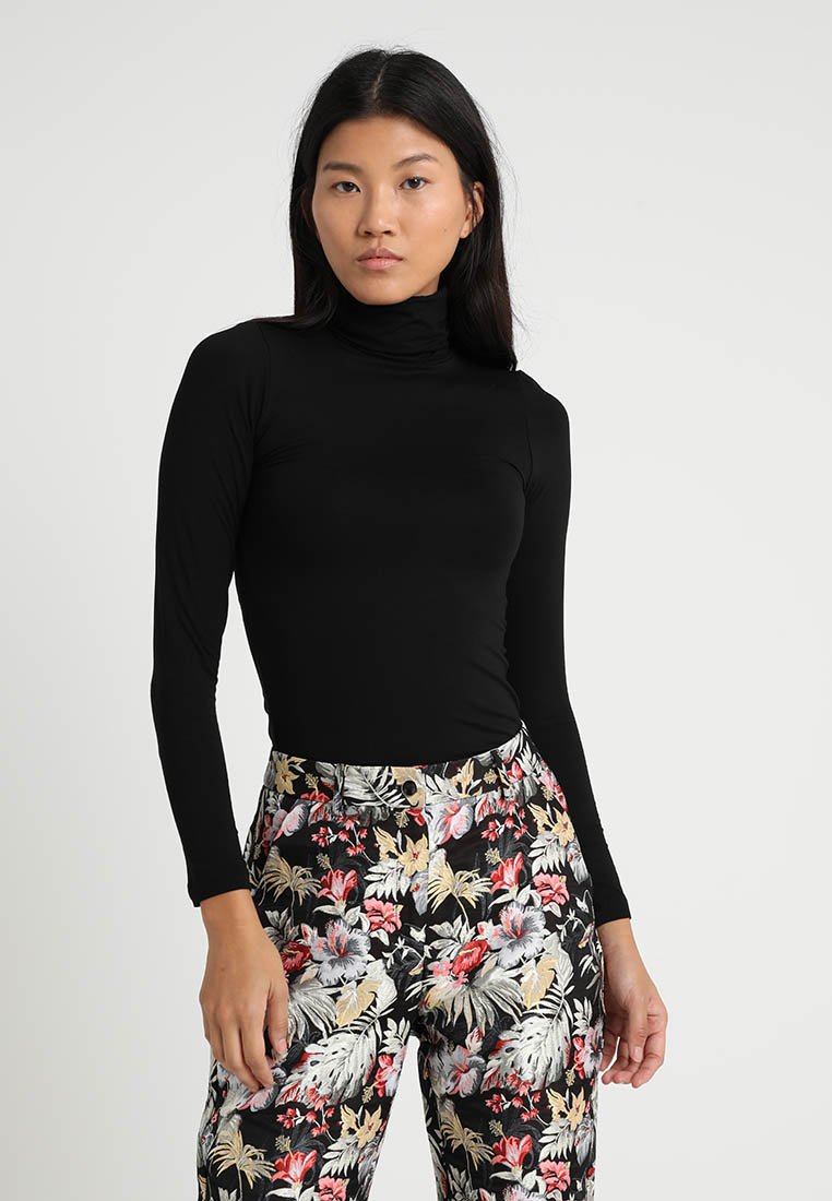 Sort langærmet turtle neck top parret med bukser med høj talje i blomsterprint med sort baggrund og farverige tropiske mønstre.