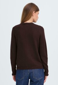 Brauner Strickpullover mit langen Ärmeln, rundem Halsausschnitt und gerippten Saumdetails. Kombiniert mit blauen Denim-Jeans, die eine schlichte Rückansicht zeigen.