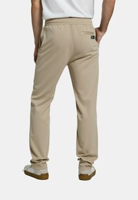 Beige joggerbroek met een elastische tailleband, gladde textuur en een achterzak. Gecombineerd met witte sneakers met een bruine zool.