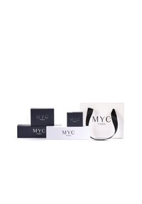 Scatole regalo in bianco e nero con "MYC PARIS" stampato in argento. Include una borsa shopping bianca con un manico nero. Diverse dimensioni e forme.
