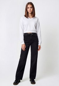 Sudadera blanca recortada con cuello en v y mangas largas, combinada con jeans negros de pierna ancha de talle alto y zapatos negros con cordones.