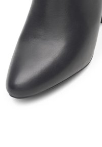 Čierne kožené vysoké topánky na podpätku s špicatou špičkou a hladkým povrchom. Dizajn sa vyznačuje čistými líniami a skromnou výškou podpätku.