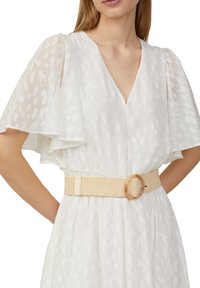Weißes Kleid mit halbtransparenten Flügelärmeln, V-Ausschnitt und strukturiertem Muster. Verfügt über einen gewobenen beigen Gürtel mit runder Schnalle.