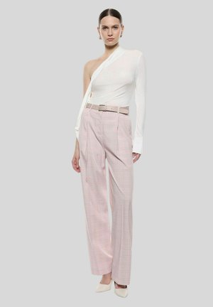 Top bianco asimmetrico con una manica lunga, abbinato a pantaloni a quadri rosa a vita alta e scarpe a punta di colore chiaro.