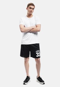 Camiseta blanca de manga corta con cuello redondo, combinada con pantalones cortos deportivos negros que presentan un gráfico en blanco que dice "LEGENDARY 33". Zapatillas deportivas negras.