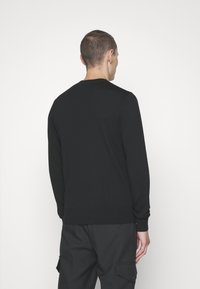 Zwarte gebreide trui met lange mouwen en een geribde zoom, gezien van achteren. Eenvoudig ontwerp, geen zichtbare patronen of hardware.