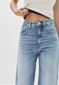 Ljust blå, högmidjade denimjeans med avslappnad passform. Har fem fickor, en framknapp och subtila blekningar över tyget.