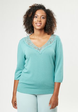 Maglione turchese con scollo a V e dettagli intrecciati in pizzo al colletto. Presenta maniche a tre quarti e orlo a coste per una maggiore struttura.