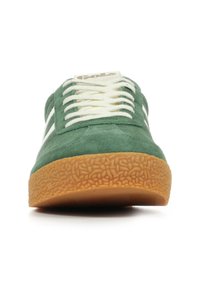 Scarpa in suede verde con strisce bianche, caratterizzata da una suola in gomma testurizzata e lacci piatti. La vista frontale mette in risalto la punta arrotondata e il branding minimale.