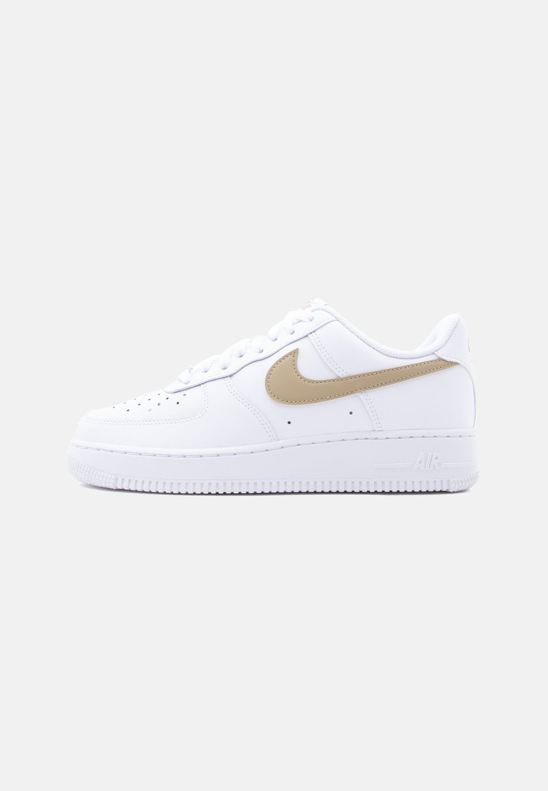 Λευκό χαμηλό παπούτσι Nike Air Force 1 με μπεζ λογότυπο swoosh, διάτρητο κουτί δακτύλων και λευκή ελαστική σόλα σε απλό ανοιχτό γκρι φόντο.