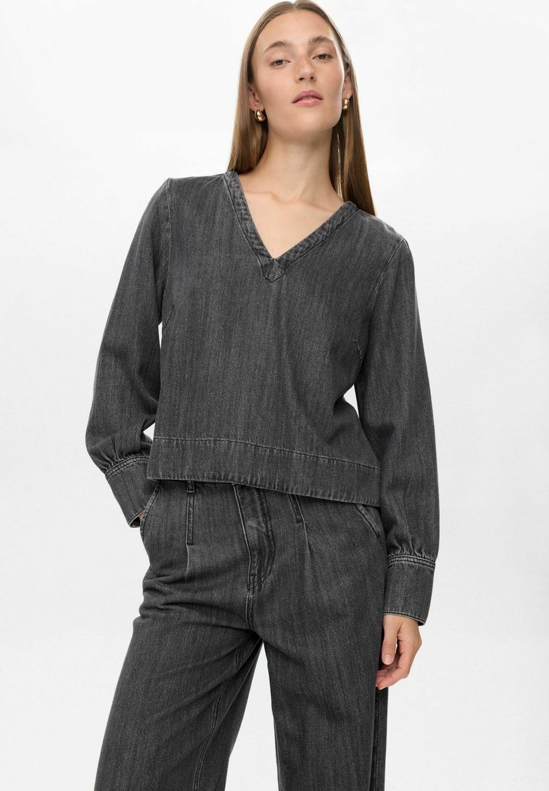 Top in denim grigio scuro con scollo a V, maniche lunghe e vestibilità cropped. Presenta dettagli di cucitura discreti e una texture liscia.