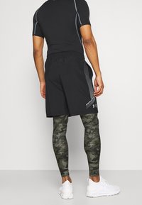 Czarna sportowa koszulka z krótkimi rękawami, lekkie czarne szorty oraz zielone legginsy w kamuflażu. Białe sneakersy dopełniają strój.