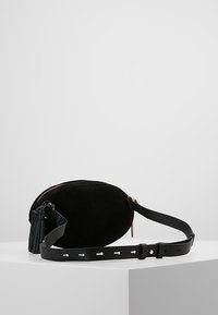 Sort oval læder taske med guld lynlås og justerbar læderrem, vist på hvid pedestal mod en ensfarvet baggrund.