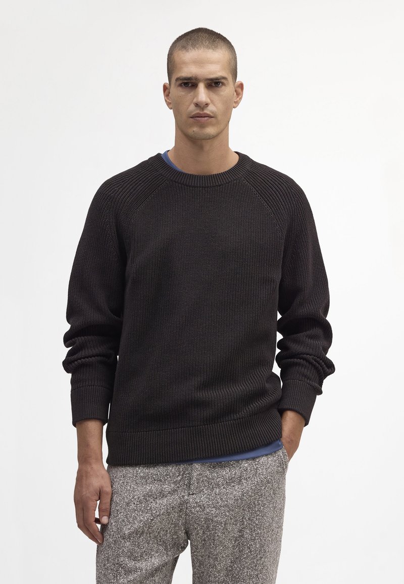 Geverfd donkerbruin gebreid sweater met een ribbelachtige halslijn en manchetten, gecombineerd met lichtgrijze geblokte broek. Eenvoudig, casual ontwerp.