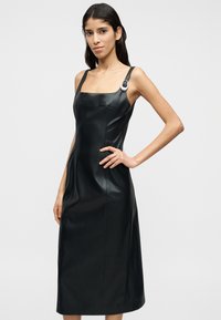 Μαύρο δερμάτινο φόρεμα με τετράγωνο ντεκολτέ, λεπτές τιράντες και ασημένια λεπτομέρεια σε μία τιράντα. Ομαλή υφή, μήκος μέχρι το γόνατο.