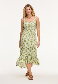 Groene jurk met bloemenprint, voorzien van een aansluitend lijfje, een gefronste zoom en verstelbare bandjes. Gemaakt van lichtgewicht stof, gecombineerd met bruine sandalen.