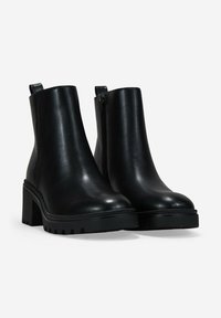 Par de botas de cuero negro hasta el tobillo con tacones cuadrados, cremalleras laterales y tiradores, mostradas sobre un fondo blanco.