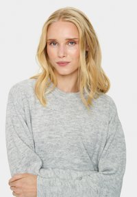 Jasnoszary sweter robiony na drutach z okrągłym dekoltem, długimi rękawami i ribbowymi mankietami, o miękkiej fakturze i subtelnych odcieniach koloru.