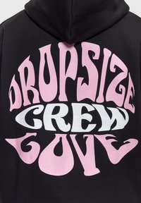 Sweat à capuche noir avec un texte rose vif ondulé « DROP SIZE » au-dessus et en dessous du texte blanc « CREW » centré dans le dos.