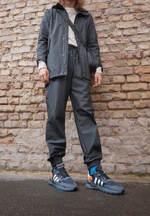 Grå vandtæt jakke med hætte, grå joggers med elastiske manchetter og blå og orange sneakers med hvide striber. Minimalistisk design.