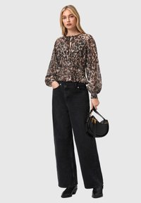 Αέρινη μπλούζα με λεοπάρ σχέδιο, με ελαστική μέση και μαζεμένα μανίκια· συνδυασμένη με ψηλόμεσα μαύρα τζιν φαρδιάς γραμμής και μικρή μαύρη τσάντα.