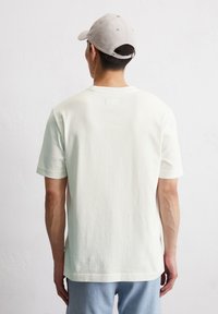 T-shirt en coton vert clair avec des manches courtes, un col rond et une petite étiquette à l'arrière. Porté avec un jean en denim bleu clair.
