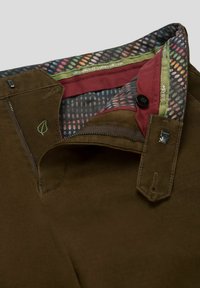 Bruine stoffen broek met een ritssluiting en knoopsluiting. Aan de binnenkant bevindt zich een kleurrijk stippenpatroon en contrasterende rode afwerking. Groen bladenlogo aanwezig.