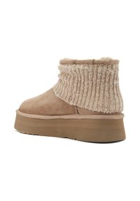 Bež nubuk čizma do gležnja s pletenim rubom, koja ima debeli, teksturirani potplat i mekanu podstavu za dodatnu udobnost.