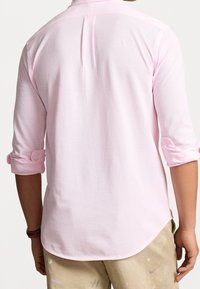 Ljust rosa långärmad skjorta med uppvikta ärmar, texturerad tyg och detalj på ryggen. Rak fåll med lätt kurvatur på sidorna.