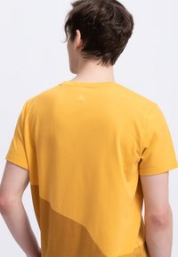 Geel katoenen t-shirt met een gebogen zoom, met een subtiele verloop; heeft een klein schaarlogo geborduurd op de hals.