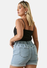 Vaaleansiniset farkkushortsit, joissa on joustava vyötärö ja kääretaskut, yhdistettynä tiukkaan mustaan toppiin. Yksinkertainen, rento muotoilu.