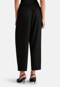 Schwarze, locker sitzende Hose mit elastischem Bund, einer glatten Textur und verkürzter Länge, kombiniert mit schwarzen Absatzsandalen.