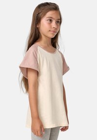 Kremfarget T-skjorte med korte ermer og lys rosa raglanermer, rund hals og myk tekstur, kombinert med grå leggings.