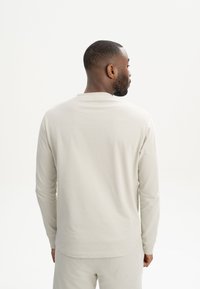 Helles graues Langarmshirt aus weichem Stoff, mit einem einfachen Rundhalsausschnitt und enganliegenden Ärmeln, das eine glatte, strukturierte Oberfläche aufweist.