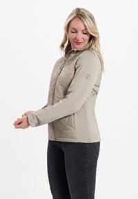 Ljusbeige puffjacka med dragkedja fram, med strukturerade vågmönster på kroppen och släta ärmar. Designad för en tight passform.