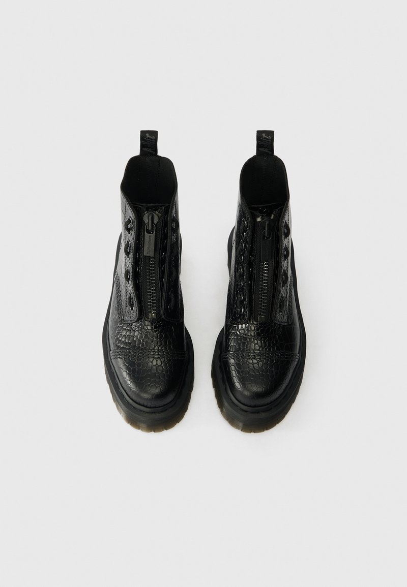 Pair of black textured leather ankle boots with zippers down the front and thick, translucent rubber soles on white background.