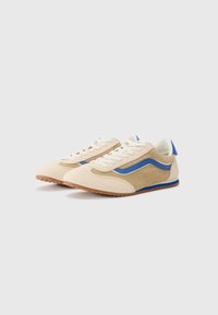 Beige og tan suede sneakers med blå sidestripe, teksturert front, hvite lisser og brun gummisåle. Rundt design på tåen.
