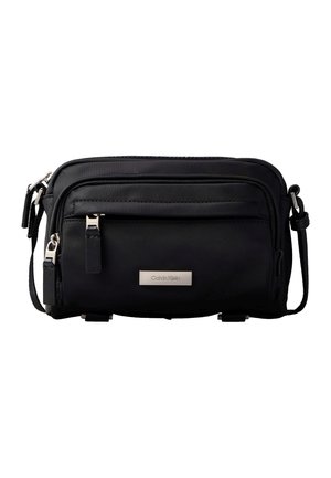 Czarna torba na ramię Calvin Klein z regulowanym paskiem, dwoma zamykanymi na suwak przedziałami i metalową plakietką z logo marki na przedniej kieszeni.