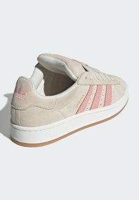 Beige suede sneaker with pink leather stripes, white rubber sole, and light pink heel accent. Features embroidered logo near heel.