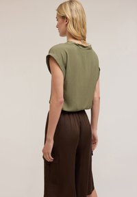 Blusa verde oliva a maniche corte, in tessuto leggero, vestibilità rilassata. Abbinata a culotte in satin marrone con una tasca applicata di lato.