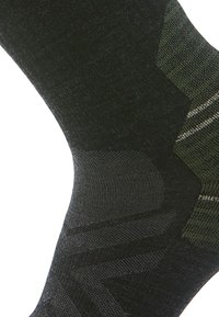 Schwarze und dunkelgrüne Socke mit einem strukturierten Strickdesign und einem geometrischen Muster, verstärktem Fersenbereich und glatter Oberfläche.