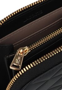 Portefeuille en cuir noir avec une texture matelassée, doté de quincaillerie dorée et d'une fermeture éclair. L'intérieur a un revêtement beige lisse.