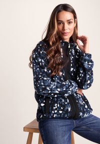 Fleece jacket with a navy base, featuring a multicolored spotted pattern. It has a high collar, zip closure, and black accents.