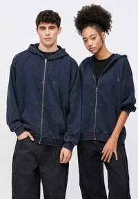 Navy zip-up hoodies with front pockets, relaxed fit, and ribbed cuffs. Paired with dark jeans, presenting a casual look.